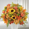Large orange and yellow arrangement with sunflowers, lilies, roses, and mums in a white vase