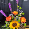Bouquet with orange roses, a sunflower, and purple spikes in a decorative vase