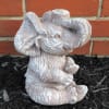 Small elephant figurine in a garden bed against a brick wall