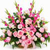 A lush, rounded basket brimming with pink roses and carnations creates an