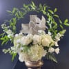 White floral arrangement with roses, hydrangeas, and a cross topper