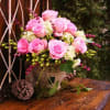 Pink roses arranged in a decorative vase with pinecones nearby