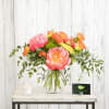 Pink and orange floral arrangement in a clear glass vase with a candle beside it