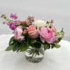 Low arrangement of soft pink and white roses and ranunculus in a clear glass vase.