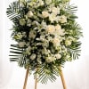 A tall, serene standing spray of white roses, lilies, and delicate orchid