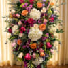A large, layered standing spray that reads as both celebratory and respectfully