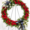 A dramatic circular wreath with dense red roses and carnations makes a