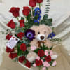 A plush teddy bear tucked into a spiral of deep red roses