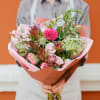 Handheld bouquet of pink and white flowers wrapped in peach paper