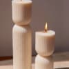 Two lit cream pillar candles with ribbed sides