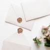 Three cream envelopes with wax seals beside pink flowers