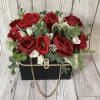 Red roses and white blooms arranged in a black box with a gold chain handle.