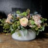 Low floral arrangement in a white container with pale roses and mixed blooms