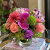 Bouquet of pink roses, orchids, and green pom-pom blooms in a glass vase