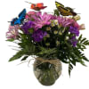 Mixed bouquet of purple and pink flowers in a glass vase with butterfly picks