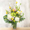 Tall mixed bouquet in a clear glass vase with yellow, white, pink, and green flowers.