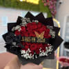 Tightly packed  red roses with white baby's breath, wrapped in black