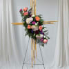 Floral cross arrangement on a stand with pink, peach, white, and purple blooms