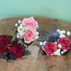 Three small rose corsages with baby's breath on a wooden surface