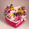 A bright heart-shaped pink box overflowing with roses, carnations, lisianthus and other