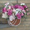 Pink and white rose arrangement in a wicker basket with pearl strands