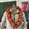 Red and yellow orchid lei draped over a beige puffer jacket on a mannequin.