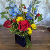 Mixed bouquet of red roses, blue flowers, and yellow daisies in a dark vase