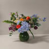 Mixed bouquet in a green glass vase with blue hydrangeas and orange roses