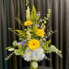 Tall bouquet of yellow gerberas, blue hydrangea, and purple flowers in a glass vase