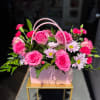Pink roses and daisies arranged in a pink handled gift box