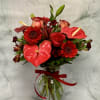 Red floral bouquet with anthuriums, roses, and gerbera daisies in a glass vase