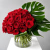 Bouquet of red roses in a clear glass vase with large tropical leaves