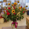 Bouquet of red roses and yellow flowers in a clear glass vase with a pink ribbon