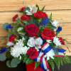 Red, white, and blue floral arrangement in a red container with ribbon
