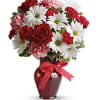 Bouquet of red roses, pink carnations, and white daisies in a red vase with a ribbon