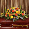 Bright orange and yellow casket spray with roses, gerbera daisies, and lilies on a wooden casket