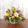 Colorful mixed flower basket with pink roses, yellow lilies, and a white gerbera on a wooden table.