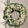 Ivory roses and white lilies arranged in a full circular wreath create