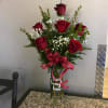 Red roses arranged in a clear glass vase with a pink ribbon