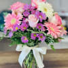 Pink roses and gerbera daisies in a glass vase with a white ribbon