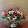 Mixed pink and burgundy flowers arranged in a silver pedestal vase