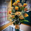 Tall bouquet of orange roses in a gold vase with a ribbon