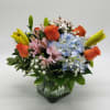 Mixed bouquet of orange roses, blue hydrangea, and yellow lilies in a glass vase