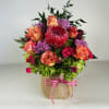 Mixed bouquet with roses, purple mums, and a red protea in a burlap-wrapped container