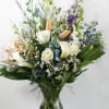 Tall mixed bouquet of white and pastel flowers with blue accents in a clear glass vase