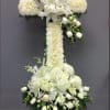 White floral cross on an easel with lilies and roses