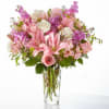 Tall clear glass vase of pink lilies, roses, white roses, and lavender blooms.