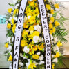 Tall yellow and white standing funeral spray with condolence ribbons on an easel.