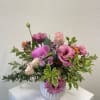 Low arrangement of pink lisianthus, roses, and mums with variegated foliage in a white ceramic vase.