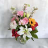 A single bold sunflower crowns a lush mix of lilies, roses, carnations